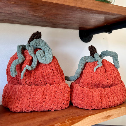 Crochet pumpkin hats sitting on a wooden shelf.